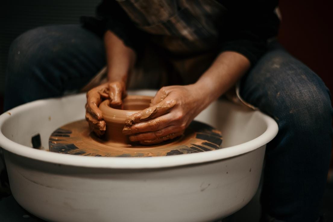 close up of a pottery wheel with someone guiding a round bit of clay with their hands
